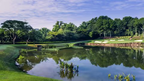 A serene pond reflecting the sky, with a lush golf course in the background, showcasing the beauty of golf in Asia.
