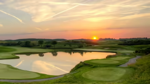 A picturesque sunset casts golden hues over a serene European golf course, creating a tranquil evening scene.