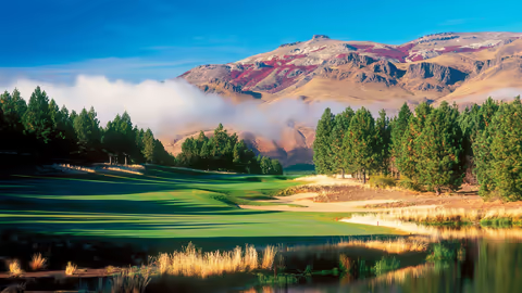Scenic golf course in the South America, framed by a majestic mountain backdrop under a clear blue sky.